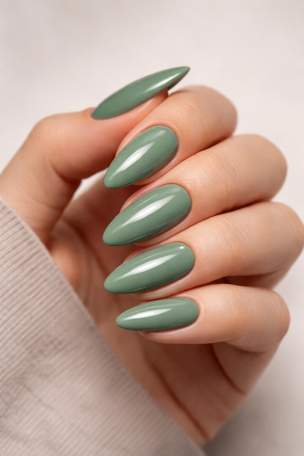 Sage green glossy almond nails with reflective finish on a neutral background