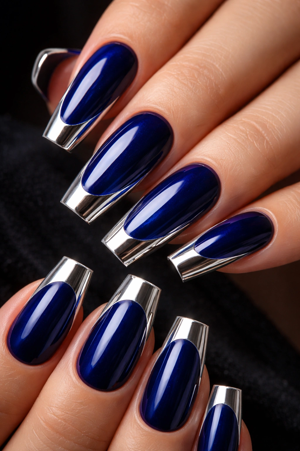 Close-up of sapphire blue coffin nails with chrome mirror-edged tips reflecting light.