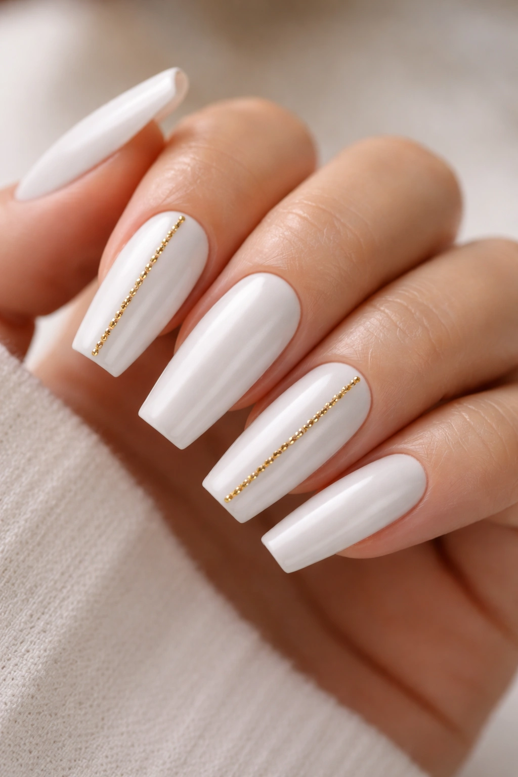 Close-up of satin white coffin nails with gold stud lines