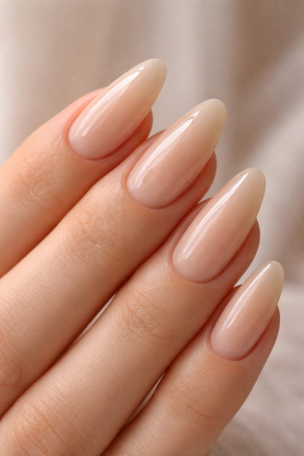 Close-up of sheer beige almond nails with a glassy finish on a hand