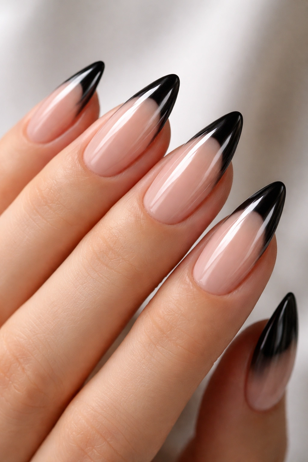 Close-up of almond-shaped nails with sheer pink base and narrow black chrome tips in studio lighting