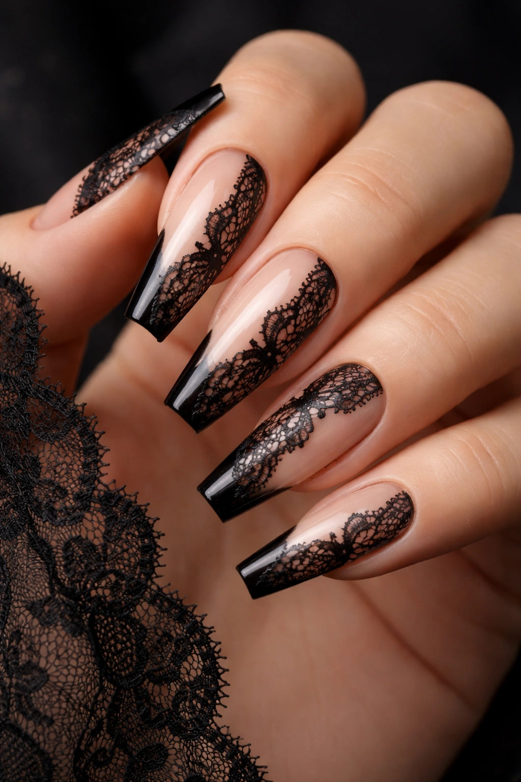 Close-up of sheer nude coffin nails with black lace panel accent on a hand