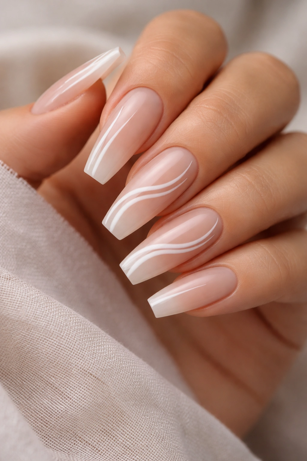 Close-up of coffin nails with sheer nude base and delicate white swirls on a soft neutral background
