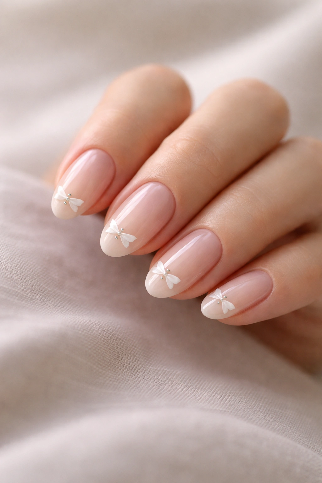 Close-up of short almond nails with a minimal bow tip on a sheer pink base