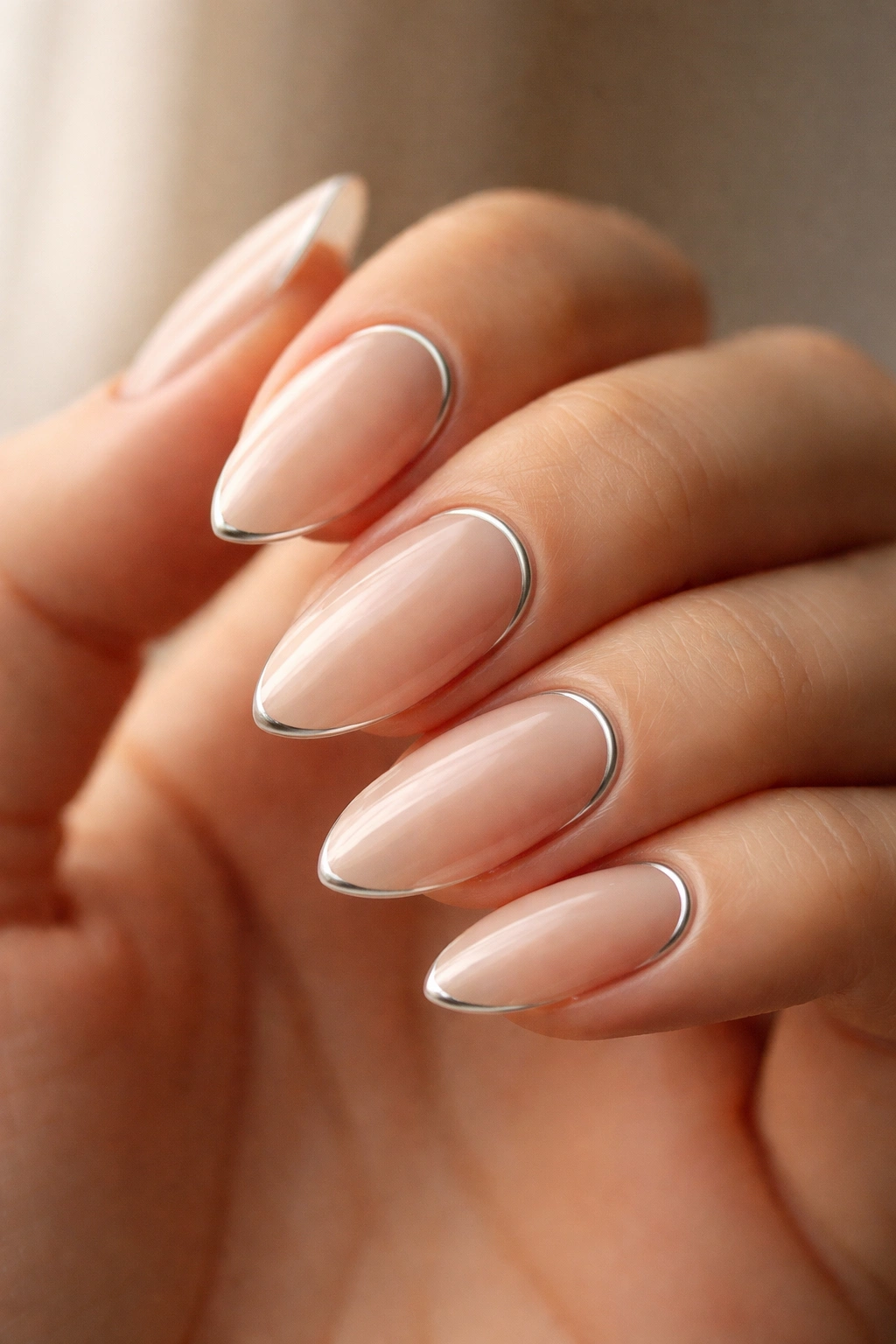 Close-up of an almond nail with a thin silver cuticle crescent on a nude base.