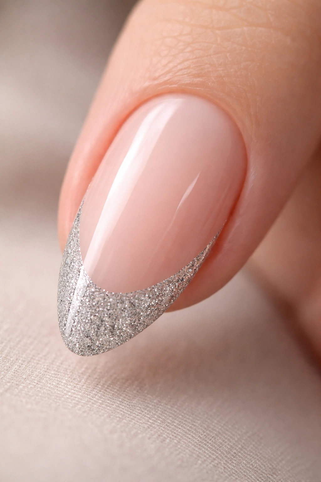 Close-up of an almond nail with a sheer nude base and a silver glitter tip along the edge