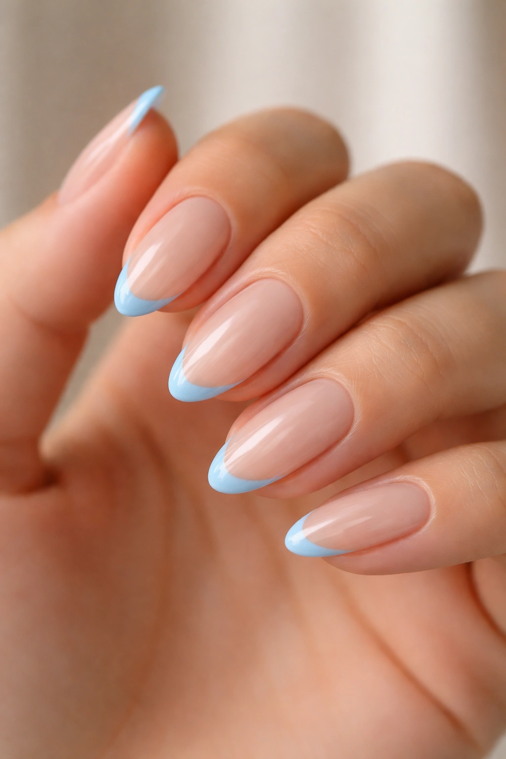 Close-up of almond nails with sky-blue micro-French tips on a sheer base