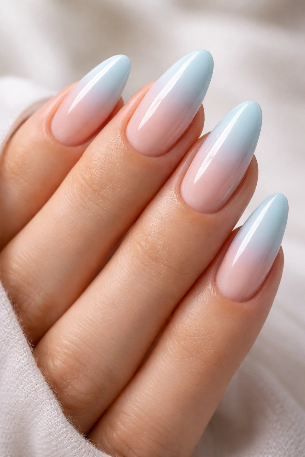 Close-up of sky blue ombre almond nails with nude base and pale blue tip