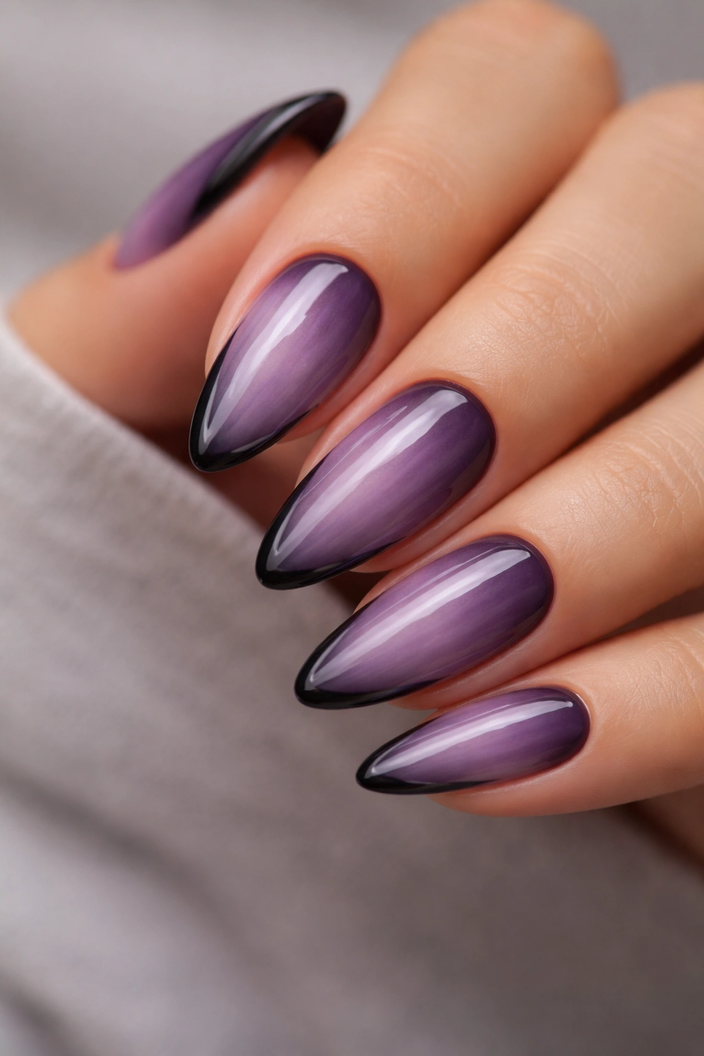 Close-up of smoky purple almond nails with an uneven black edge, moody studio lighting