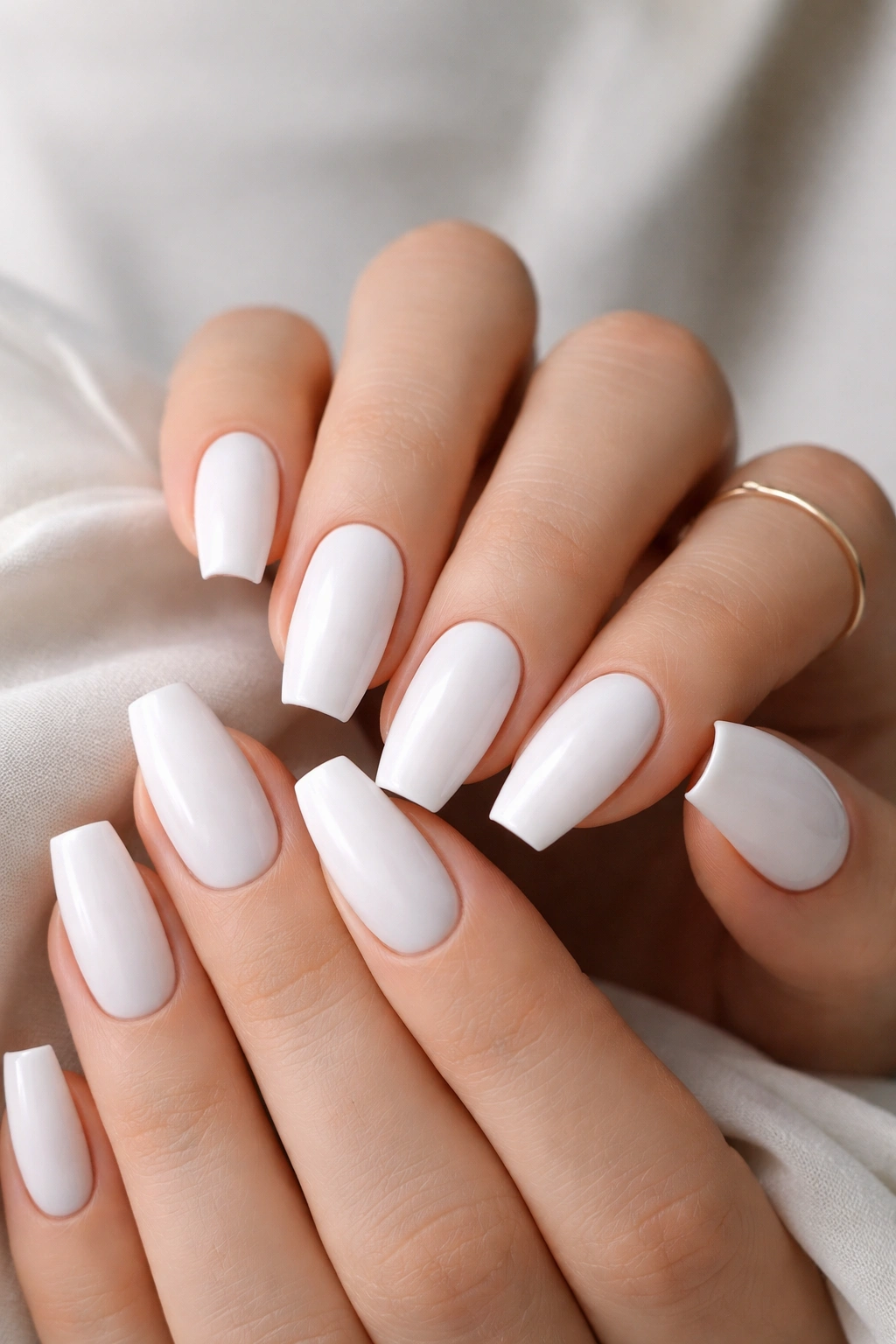 Close-up of medium coffin nails in soft baby white on hands with neutral background