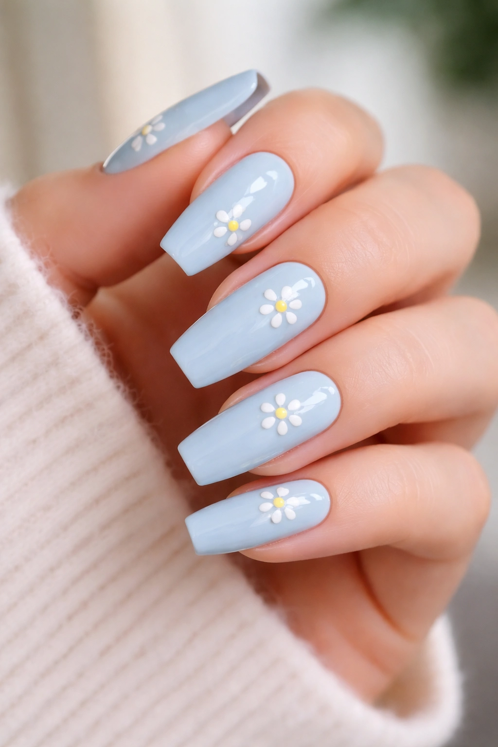 Close-up of soft blue coffin nails with daisy-style white dot clusters and yellow centers