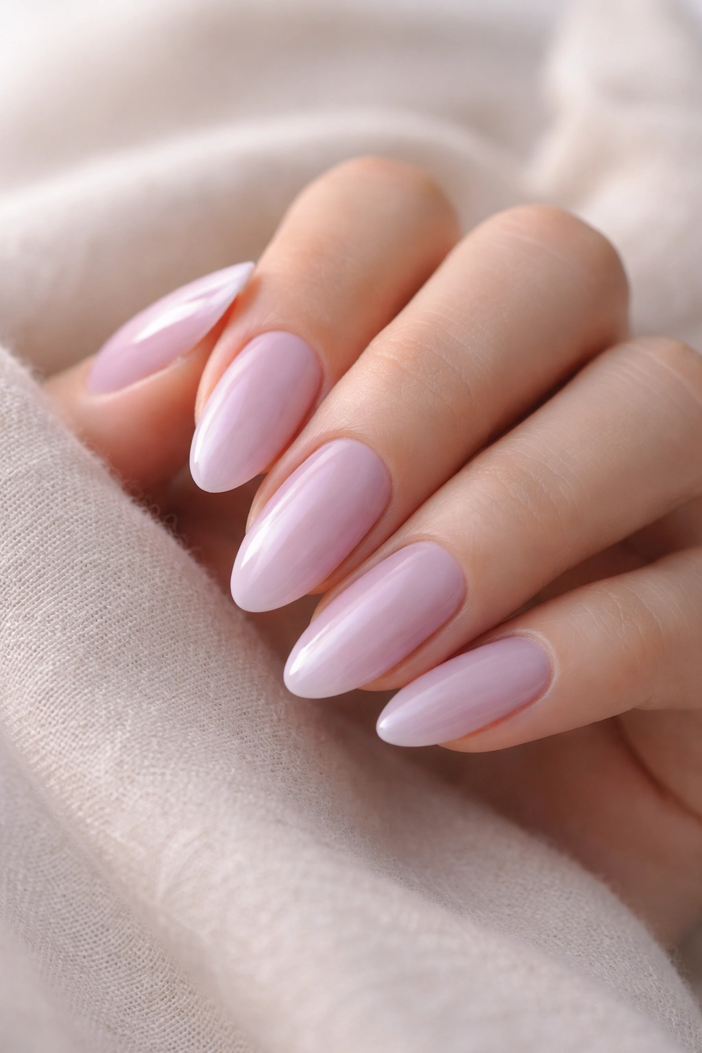 Close-up of almond nails with soft lilac gloss and nude base.