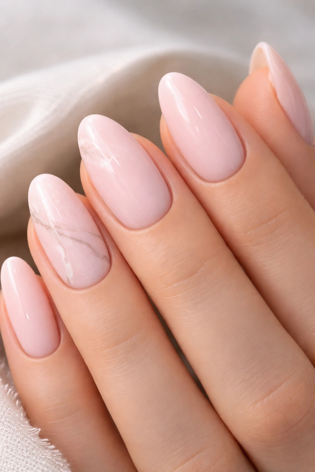 Close-up of almond nails with milky pink polish and delicate marble veins