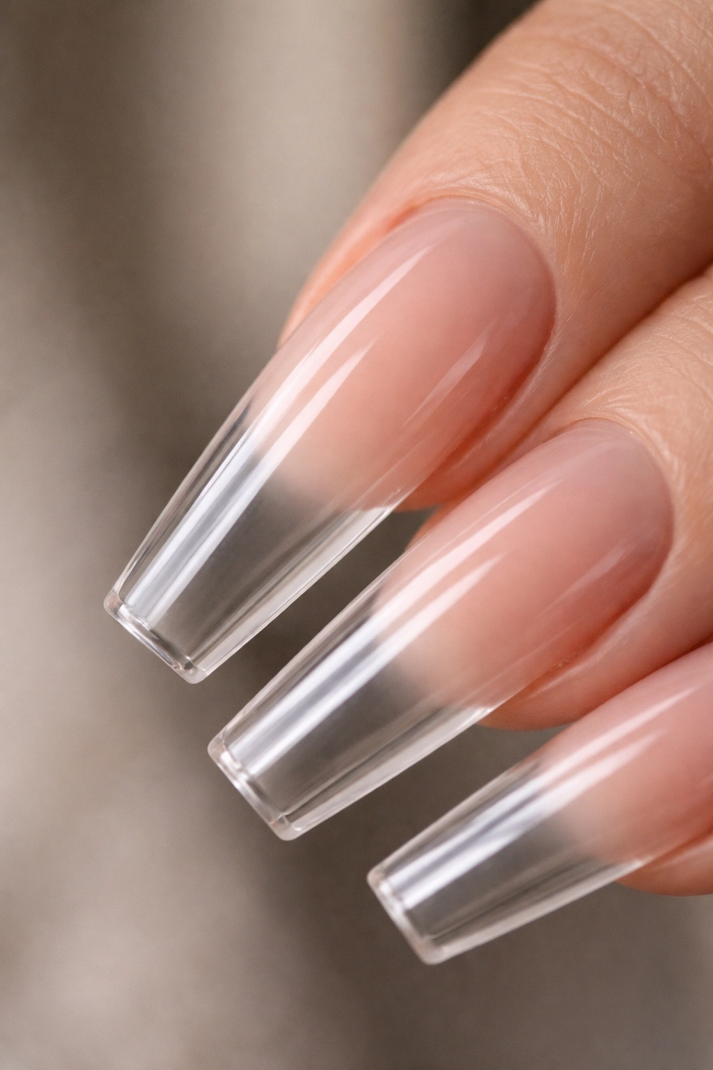 Close-up of a coffin nail with a soft nude base fading into clear length at the cuticle