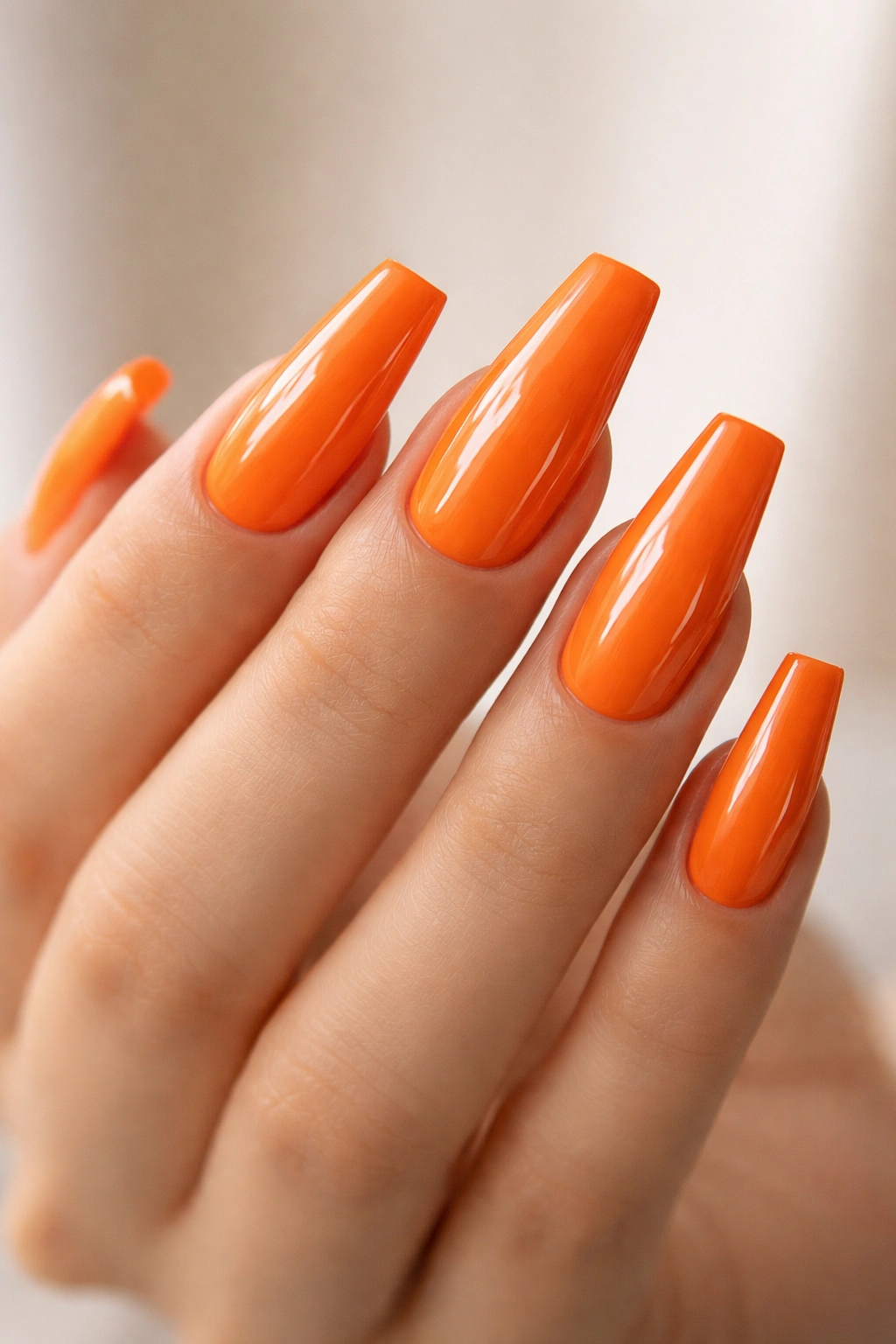 Close-up of glossy tangerine orange coffin nails on a hand with a high-shine finish