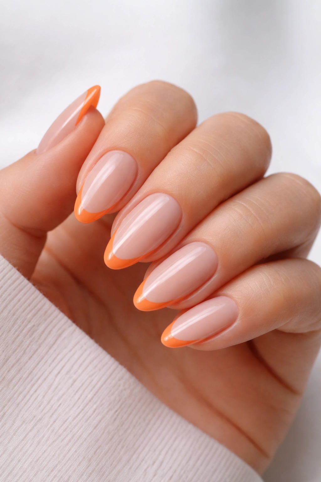 Close-up of tangerine micro-French almond nails with a slim orange tip on nude base