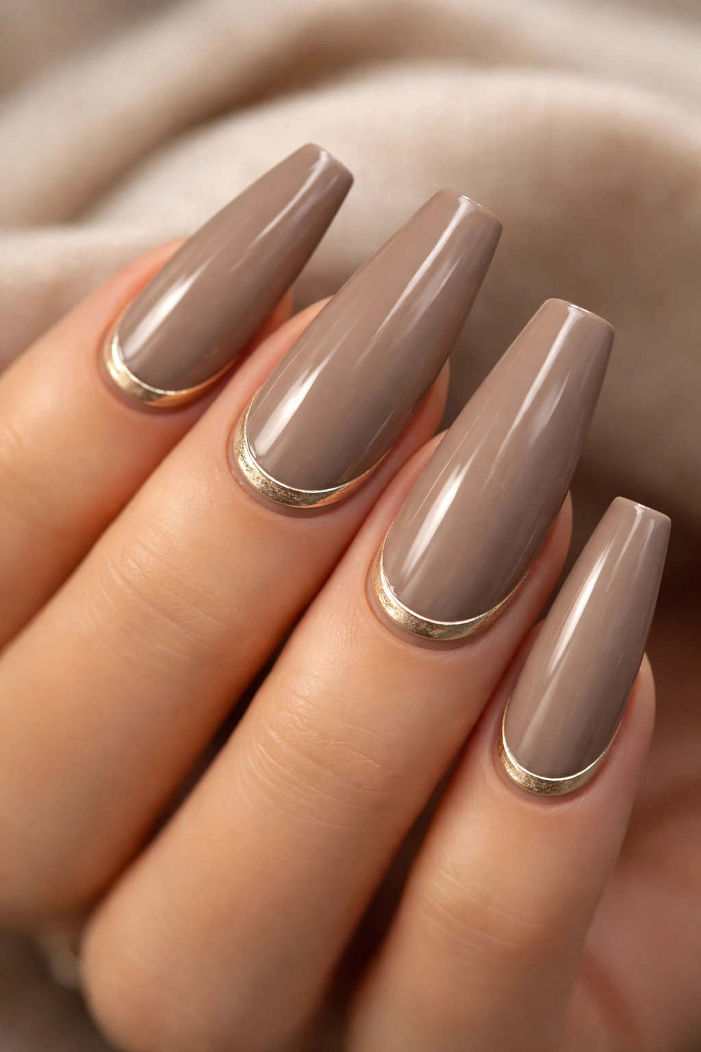 Close-up of taupe coffin nails with glossy cuticle cuffs on a neutral background