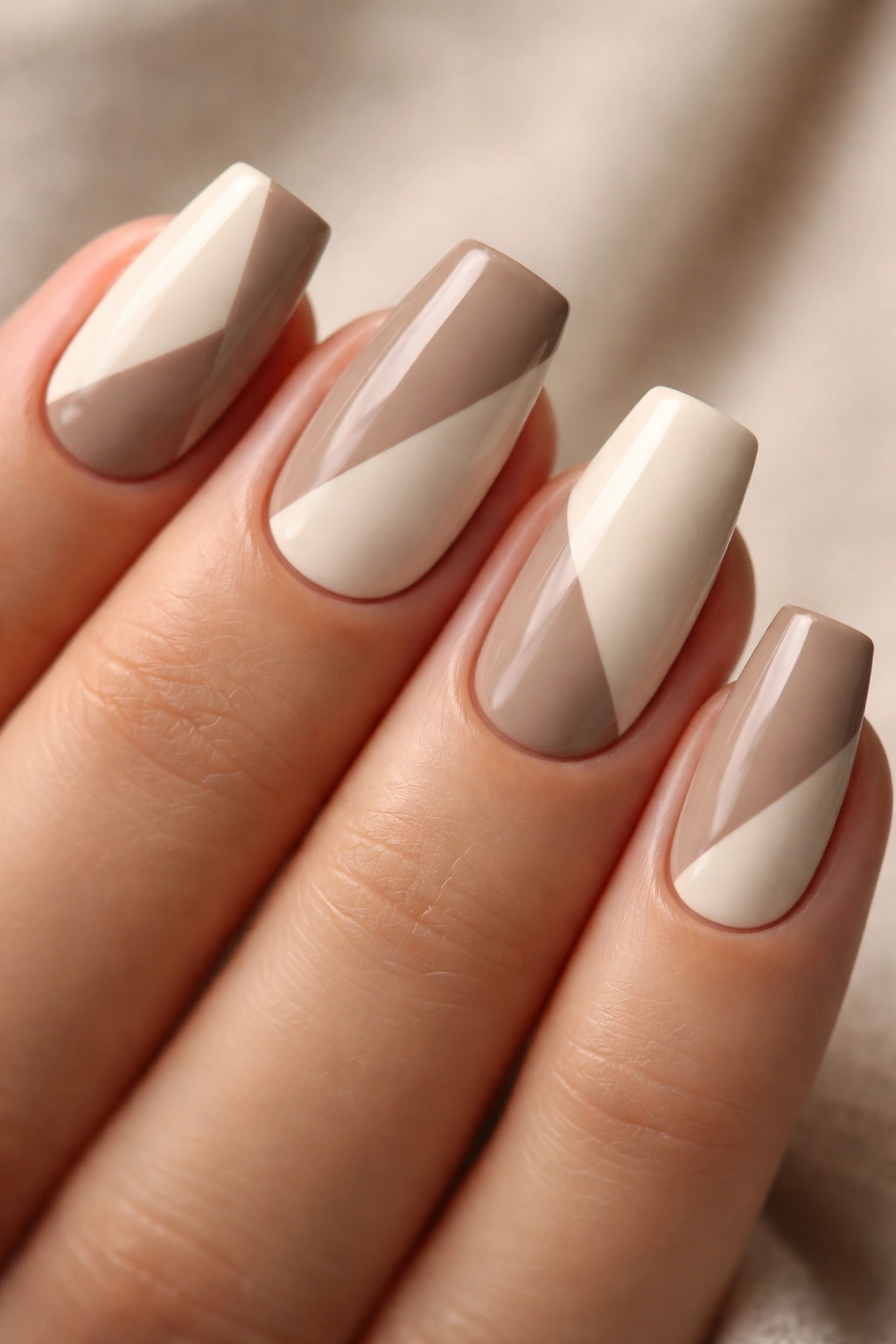 Close-up of taupe and cream color-block coffin nails on short length with crisp diagonal division.