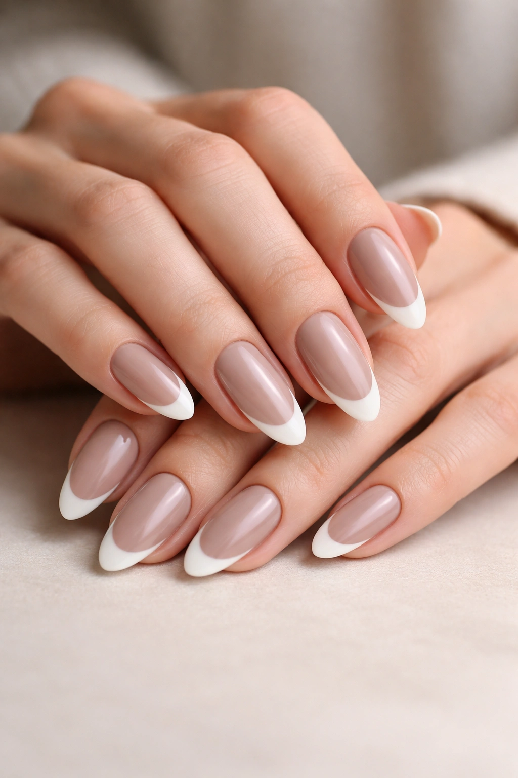 Close-up of almond nails with taupe base and ivory tips on a neutral background.