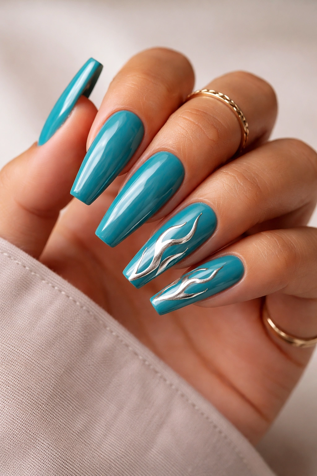 Teal coffin nails with abstract silver flames on a hand