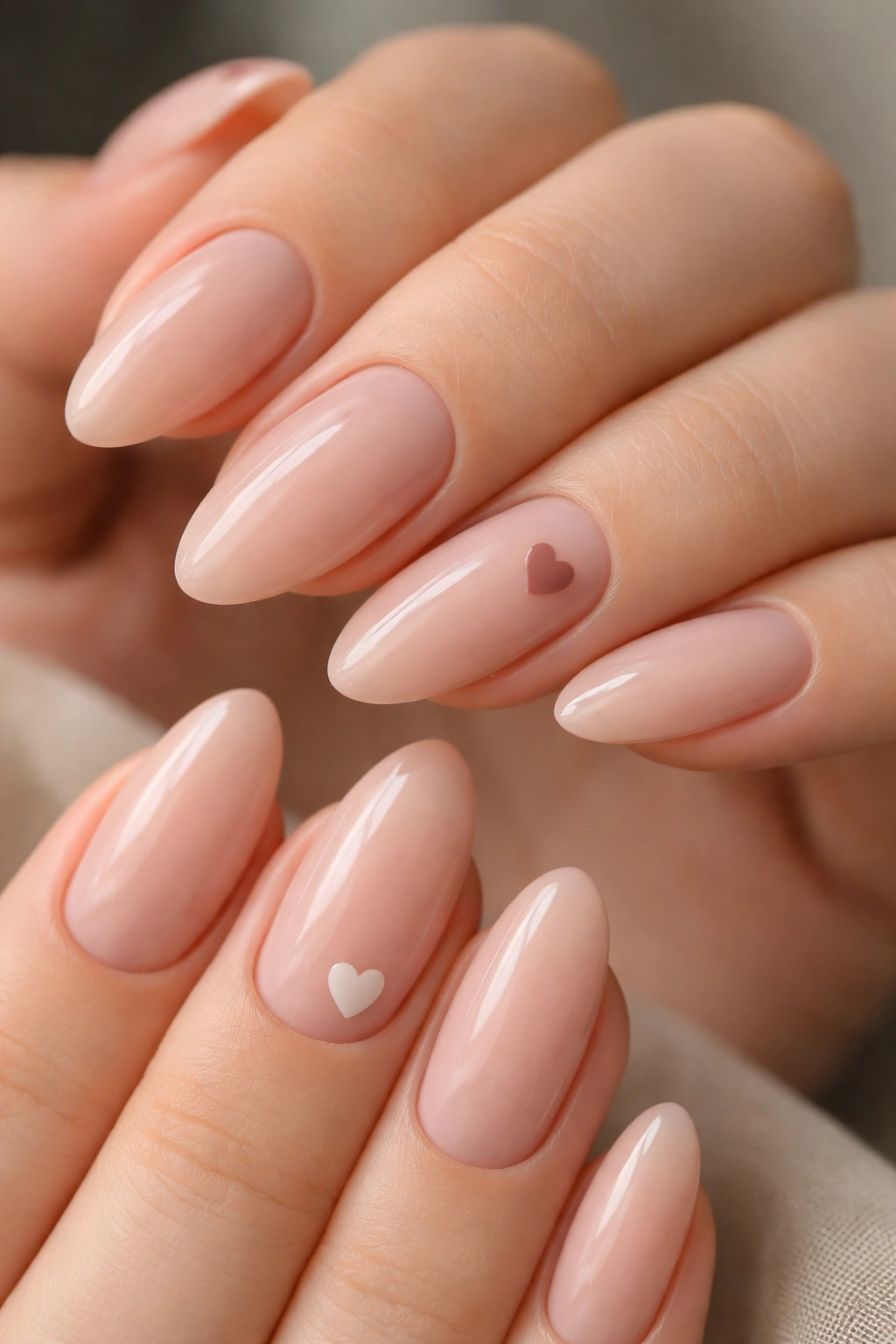 Nude almond nails with a tiny heart accent on one nail