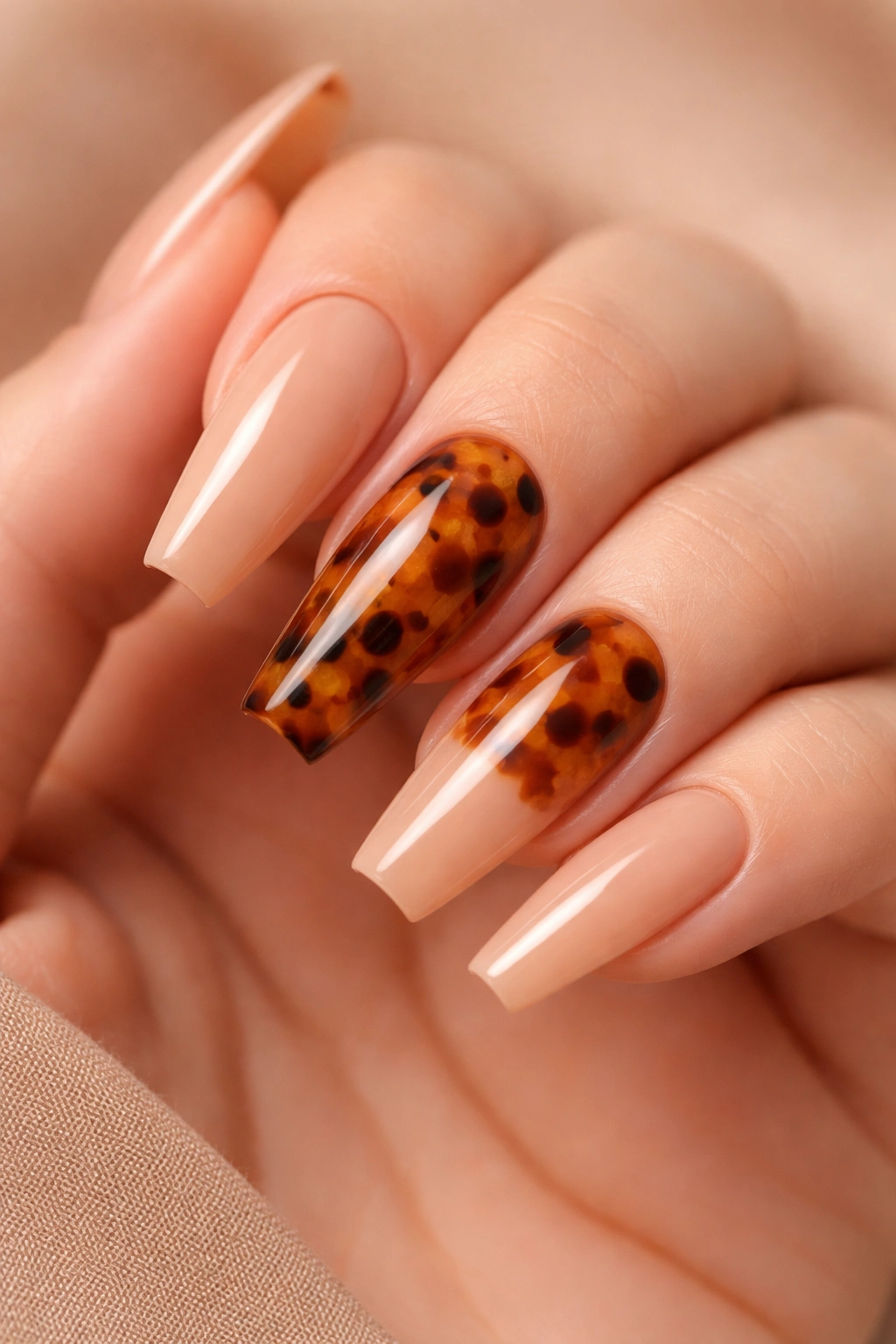 Close-up of tortoiseshell accent coffin nails on a warm nude base