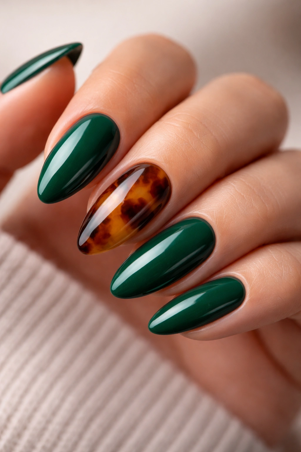 Emerald almond nails with tortoiseshell accent nail on a neutral background