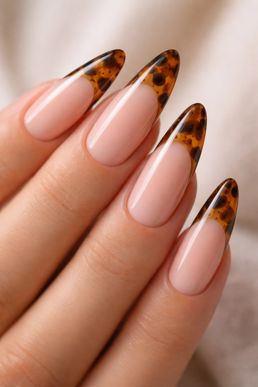 Close-up of long almond nails with tortoiseshell tips consisting of translucent brown and amber layers with irregular spots.