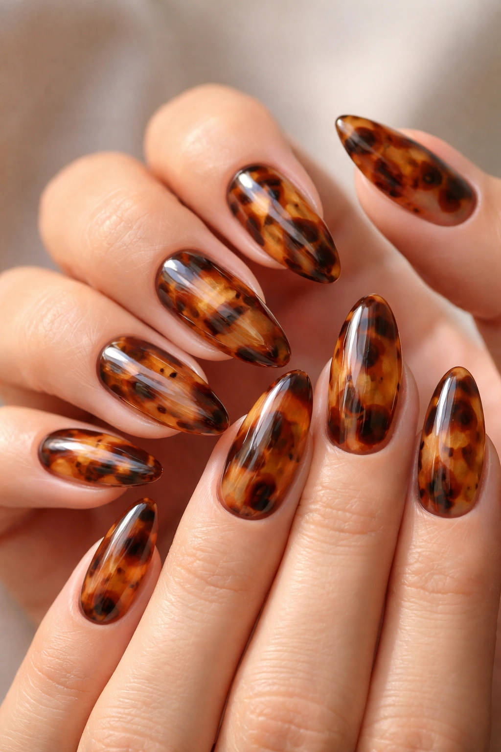Close-up of hands with tortoiseshell almond nails showing warm pattern and veining.