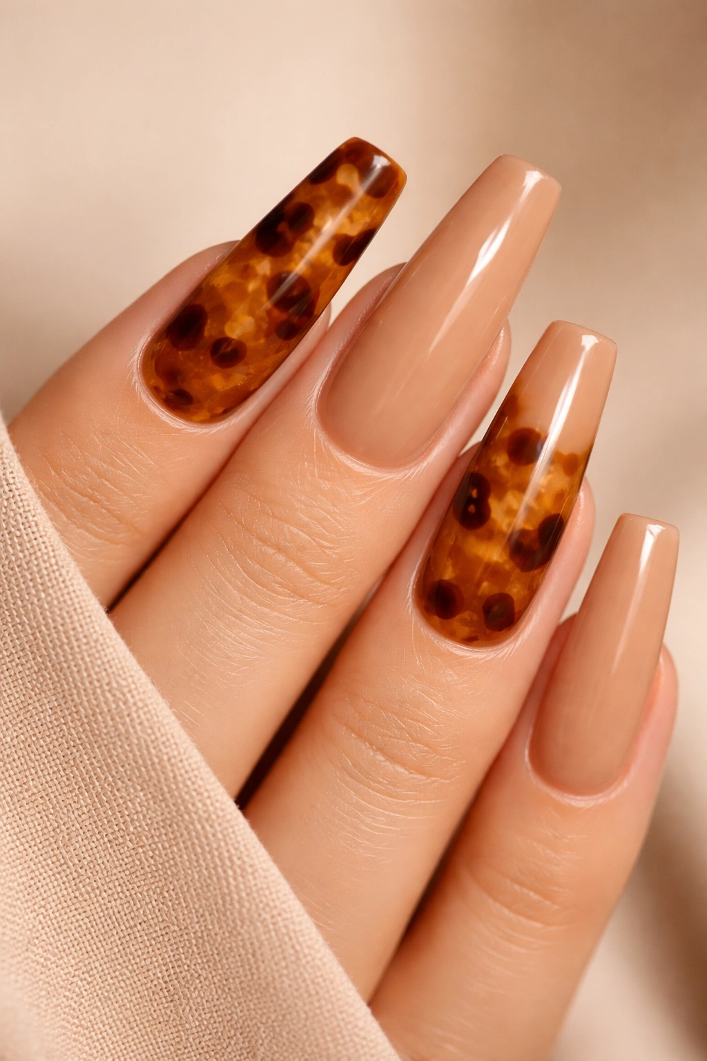 Close-up of tortoiseshell accent coffin nails on a caramel nude base with glassy depth