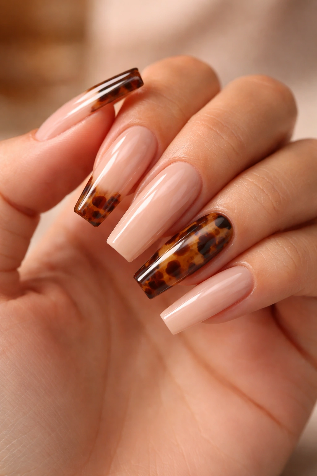 Nude coffin nails with tortoiseshell tips on a hand, warm amber-brown depth