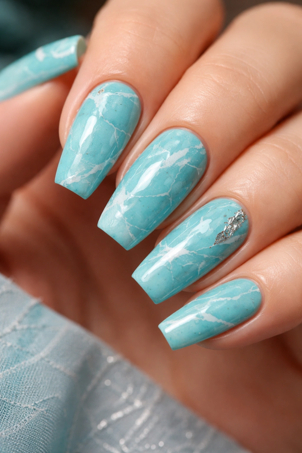 Close-up of turquoise marble nails with white veining on coffin nails