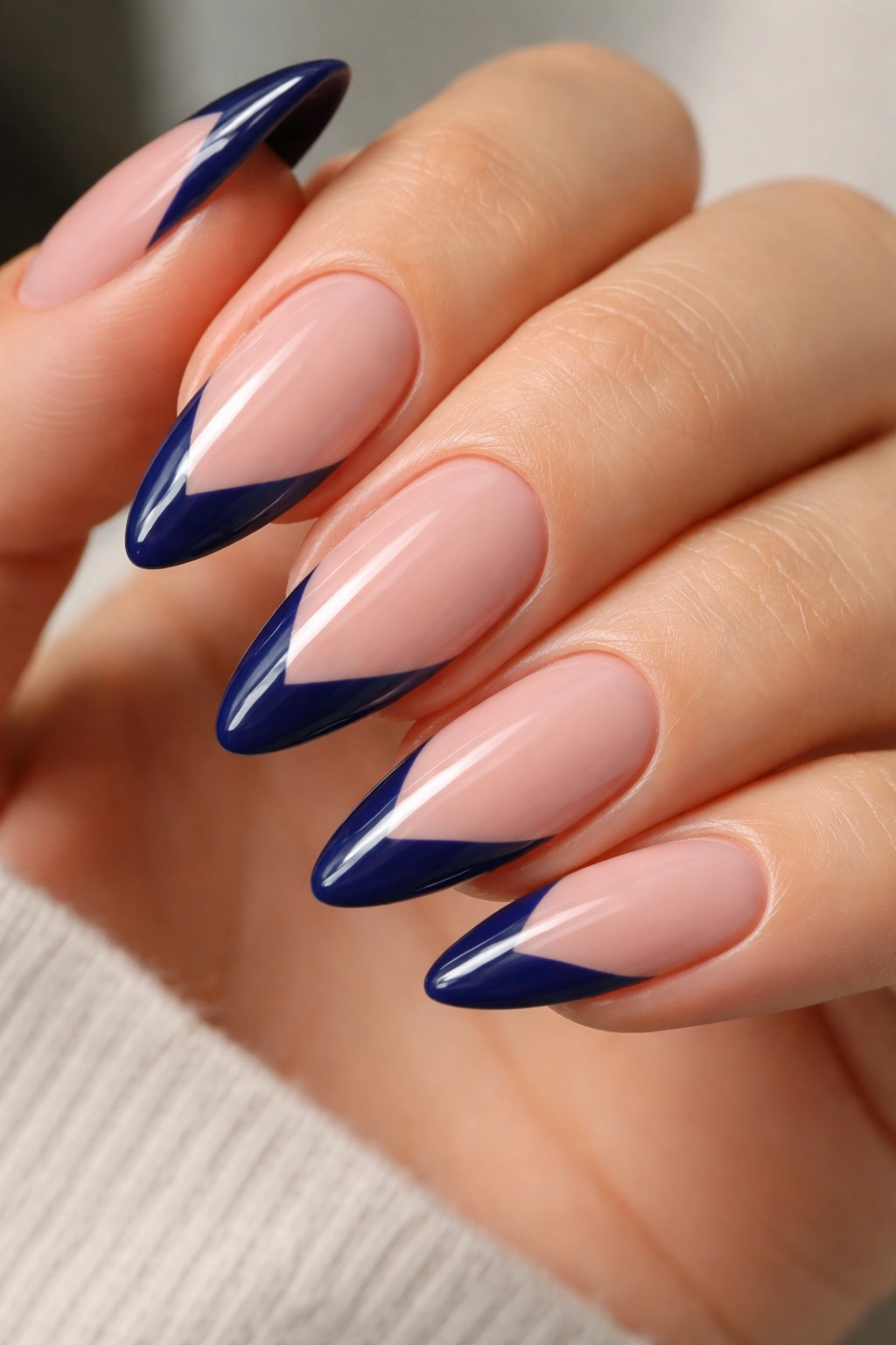 Almond nails with navy V-cut blue tips on a nude base