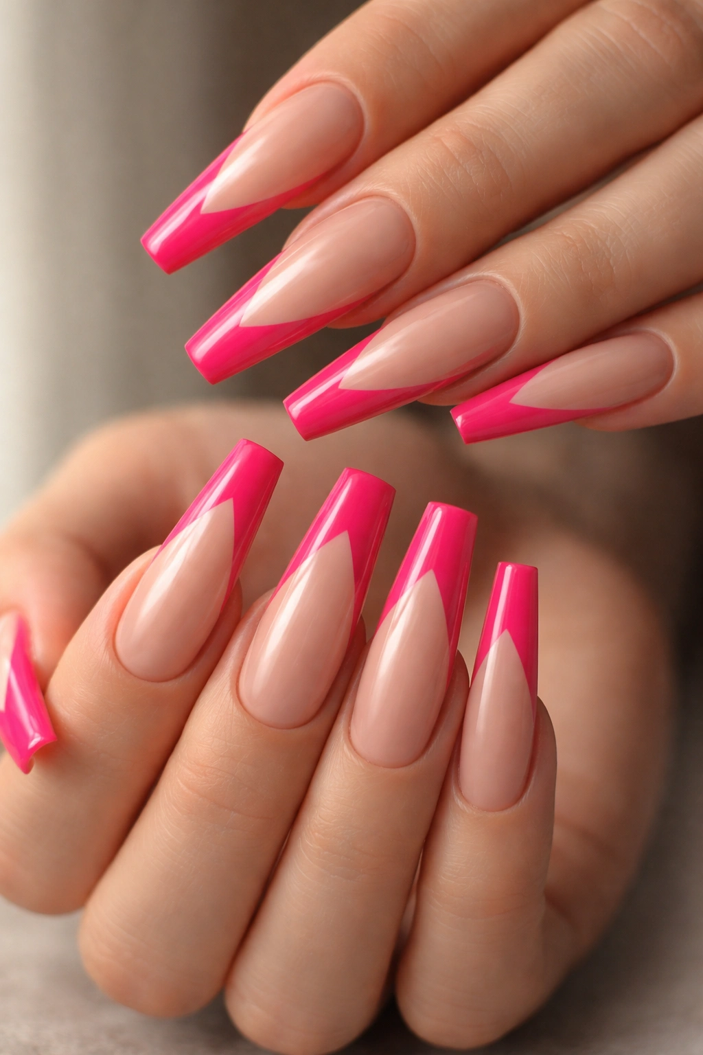 Close-up of long coffin nails with V-shaped hot pink tips on a neutral backdrop