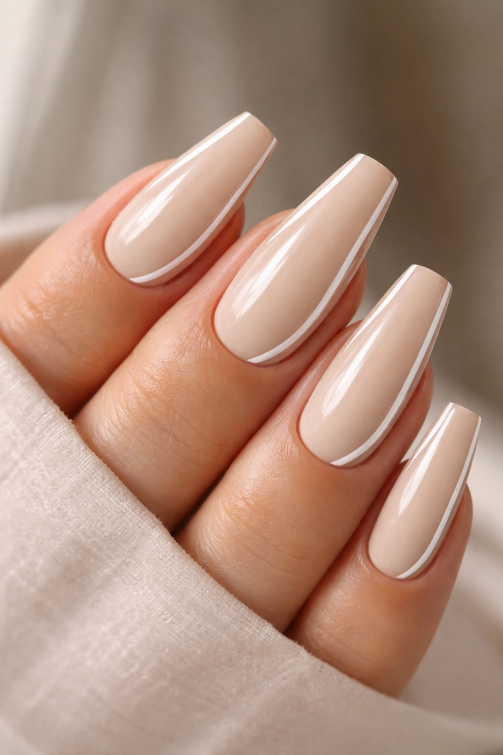 Close-up of vanilla beige coffin nails with a thin side French line on a neutral background