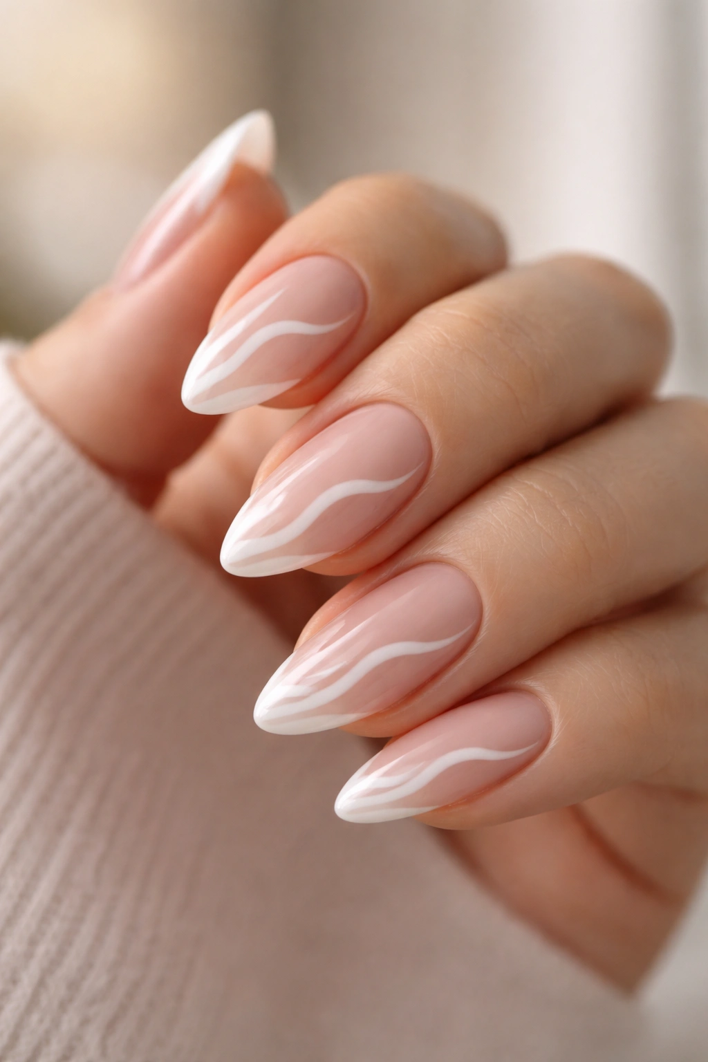 Close-up of almond nails with irregular wavy white French tips on nude base