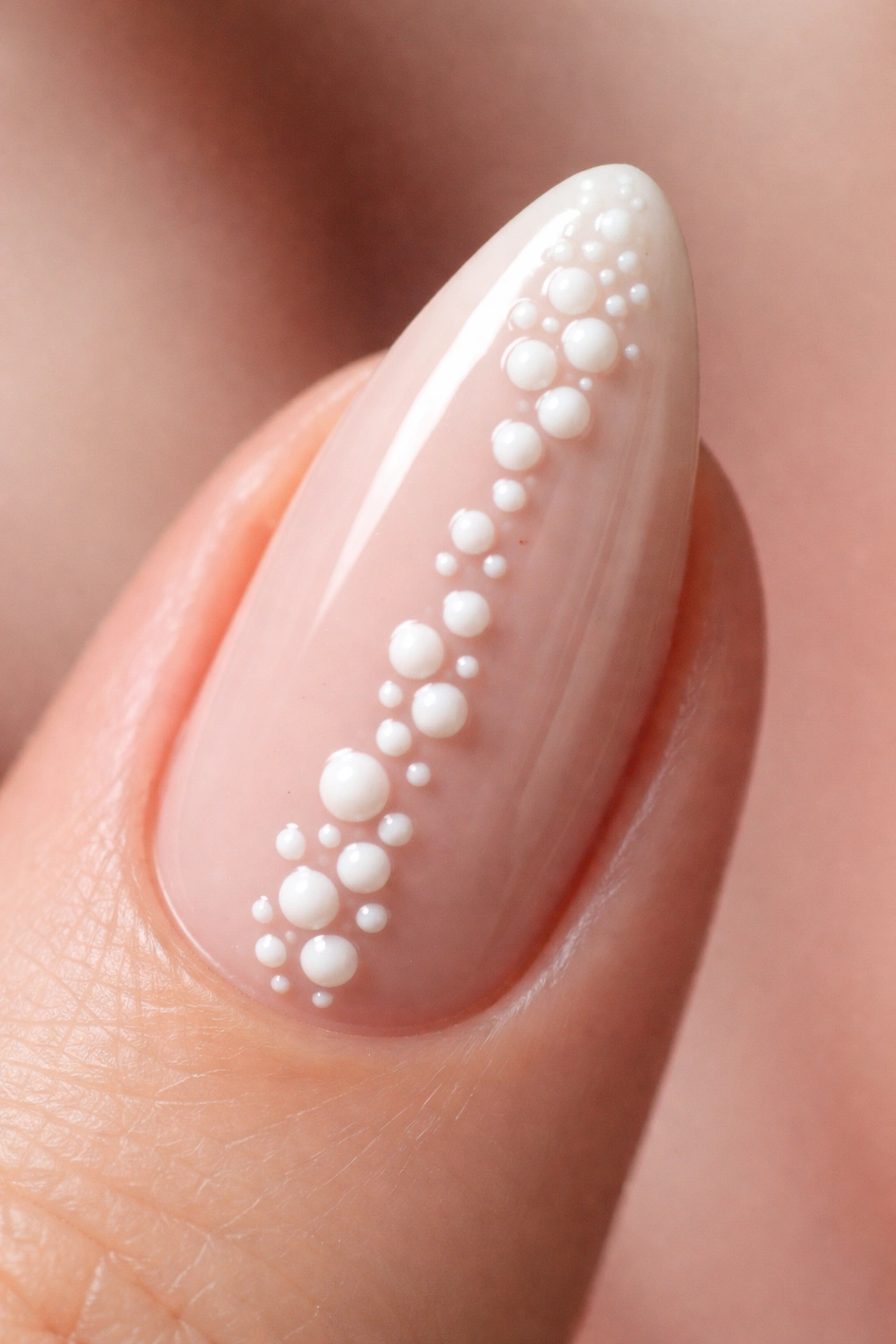 Close-up of an almond nail with small white 3D gel dots on a nude base
