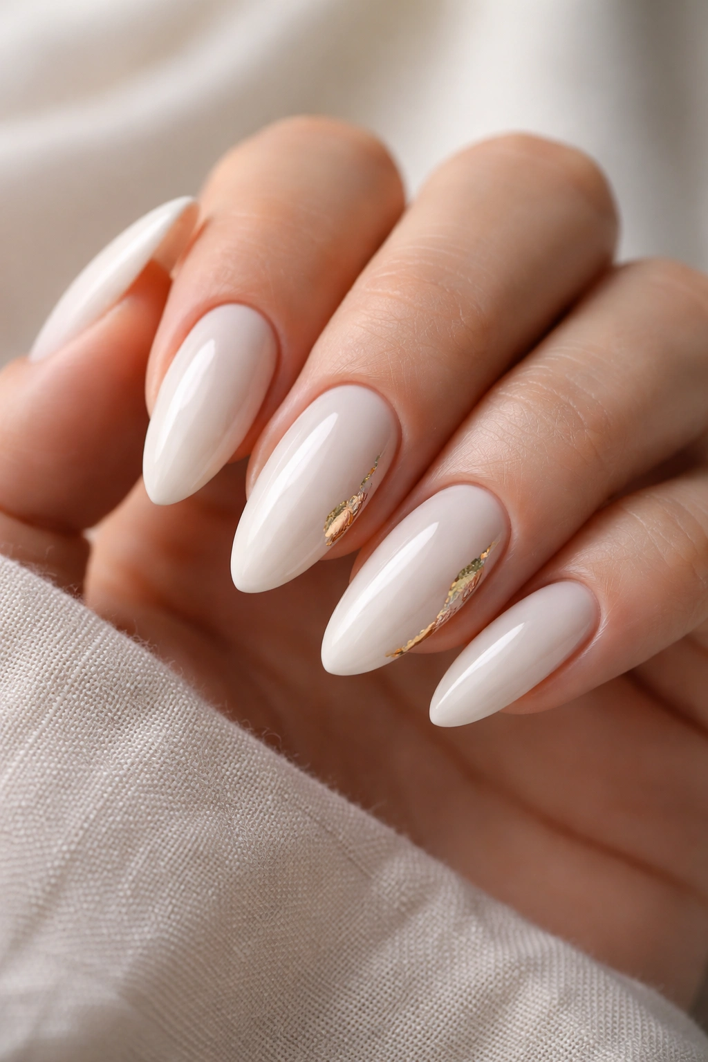 Close-up of white almond nails with subtle gold foil accents on milky base