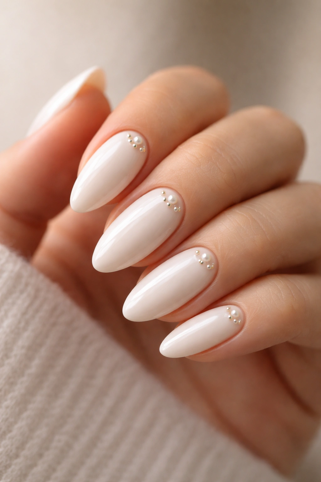Close-up of glossy white almond nails with tiny pearls near the cuticle