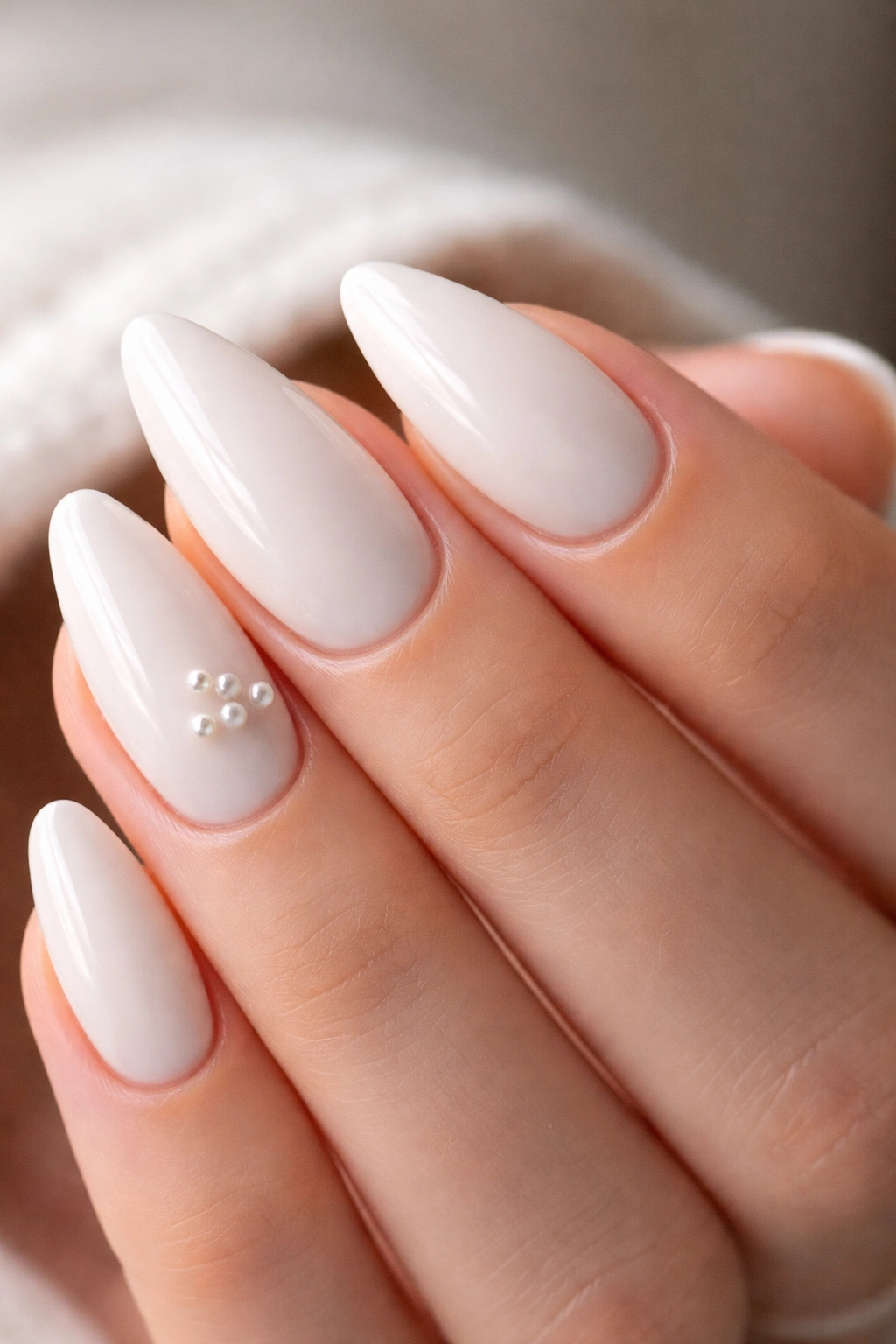 Close-up of white almond nails with tiny pearls near the cuticle on accent nails
