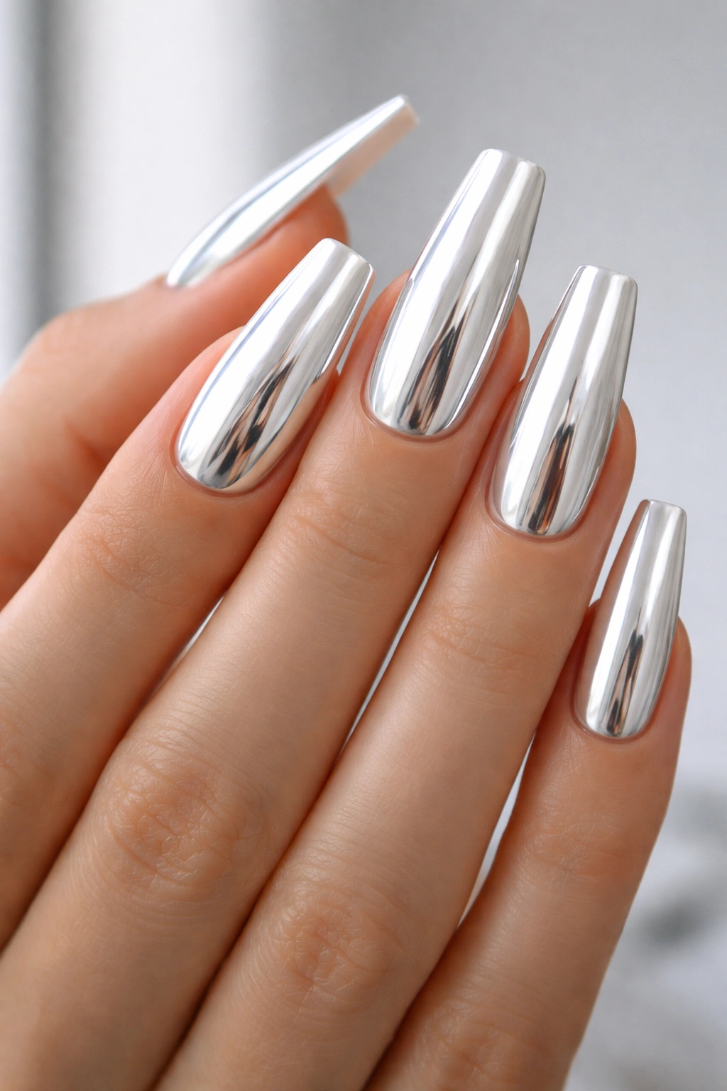 Close-up of coffin nails with reflective white chrome finish on a hand against a light background