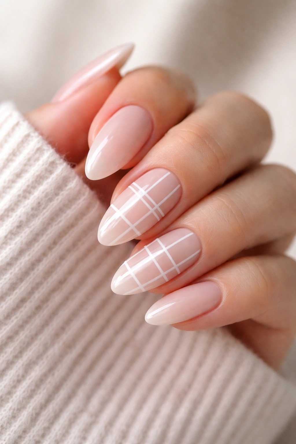 Close-up of almond nails with white grid lines on a nude base