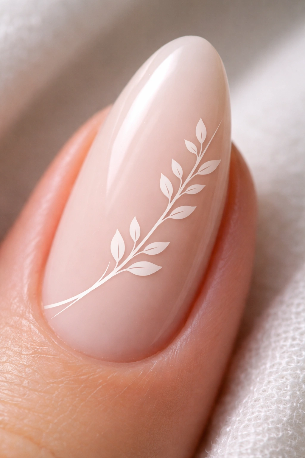 Close-up of an almond nail with a white leaf branch and tiny leaves on a nude base
