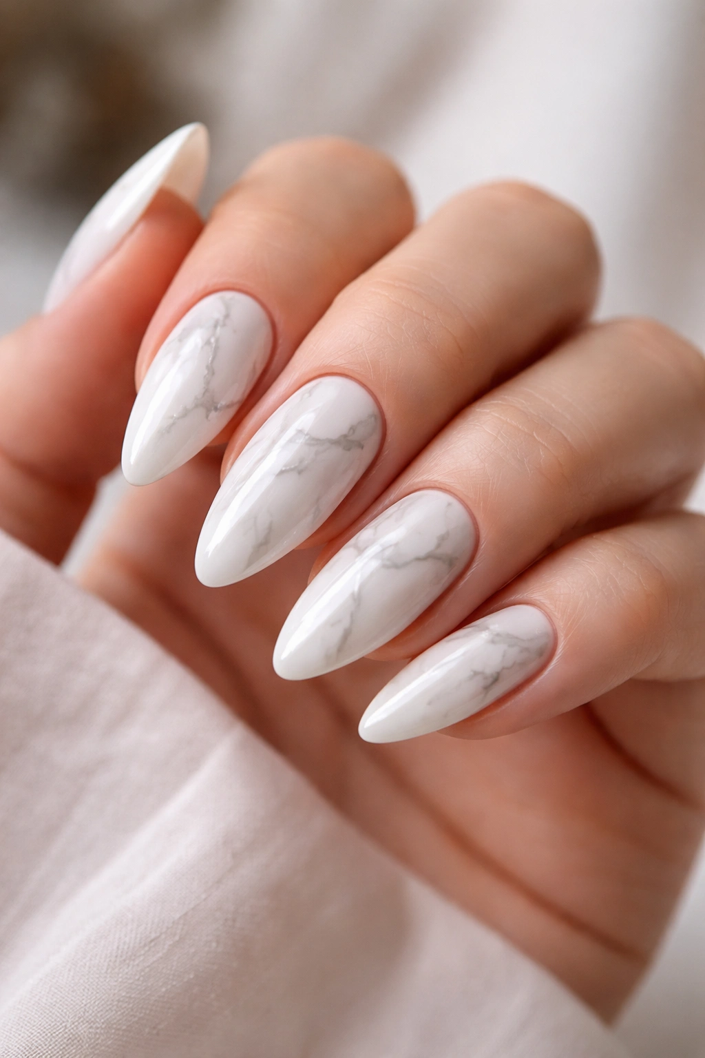 Close-up of white marble almond nails with pale gray veining and glossy finish
