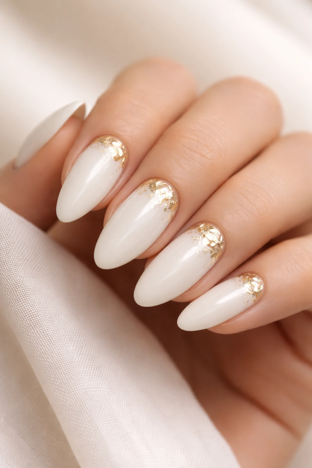 Close-up of white almond nails with subtle gold foil accents near the cuticle