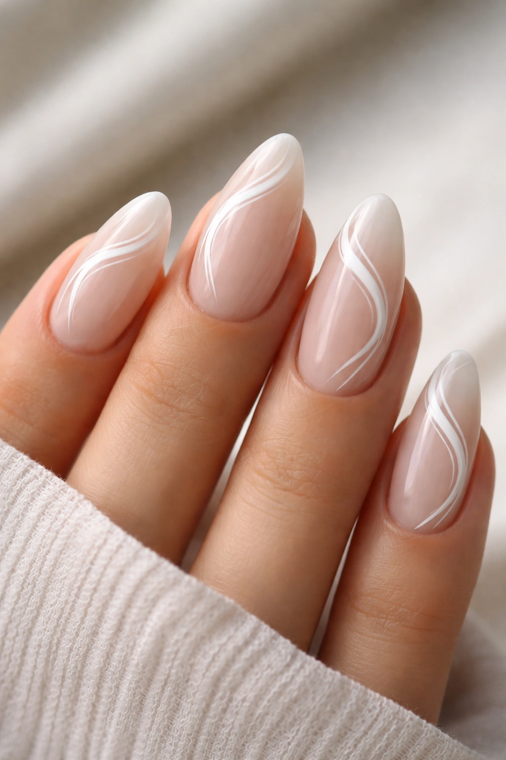 Close-up of almond nails with thin white swirl tips on a nude base