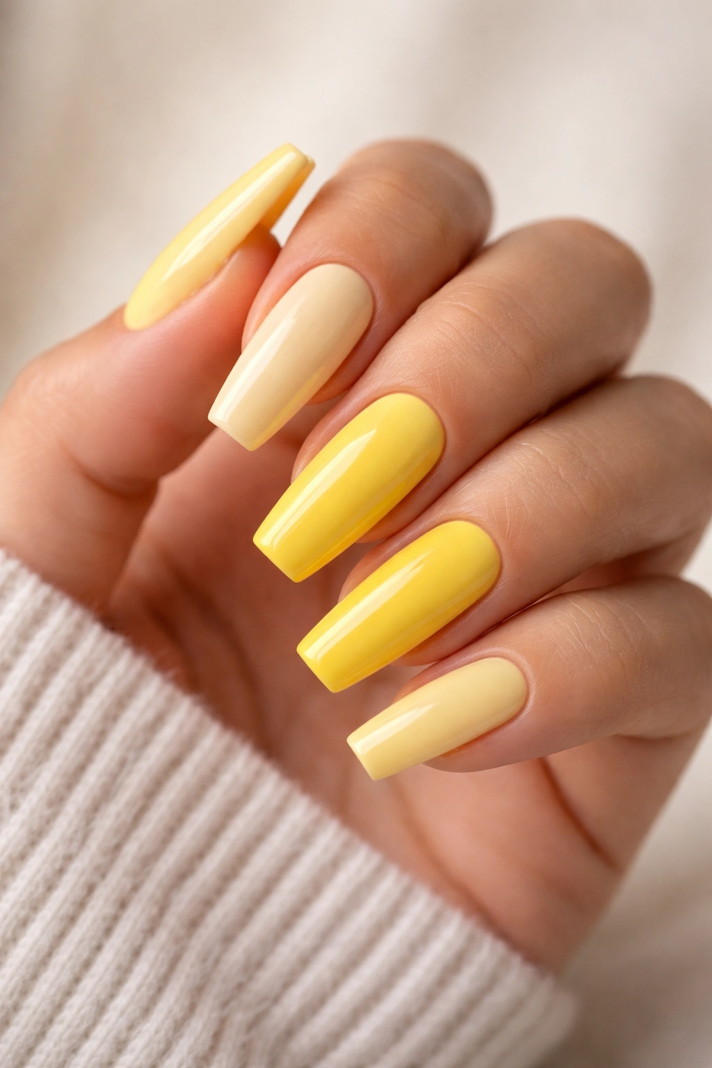 Close-up of yellow coffin nails on a hand, creamy pastel to lemon shades in a coffin shape