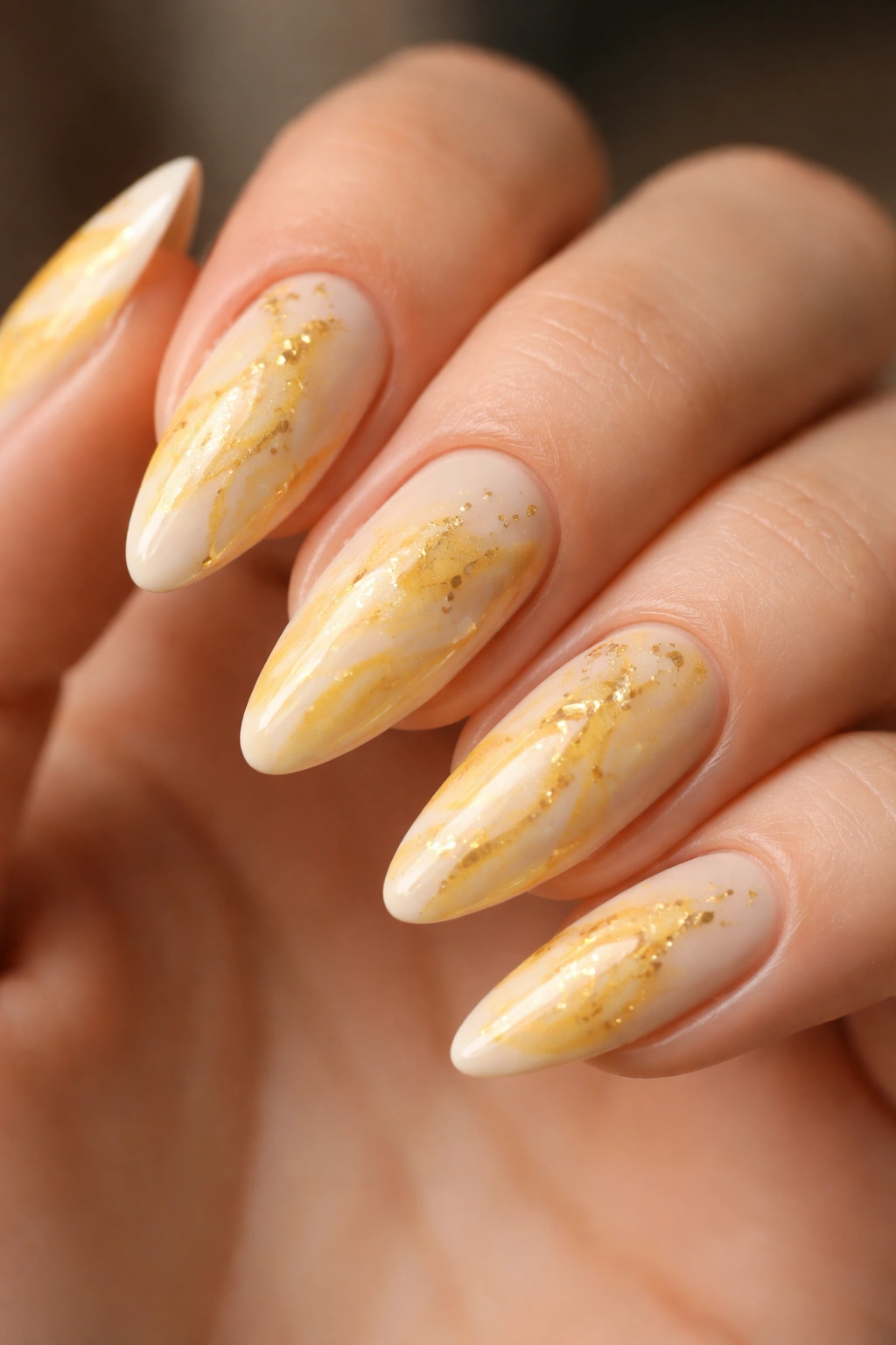 Almond nails with pale cream base, yellow marble swirls and gold foil