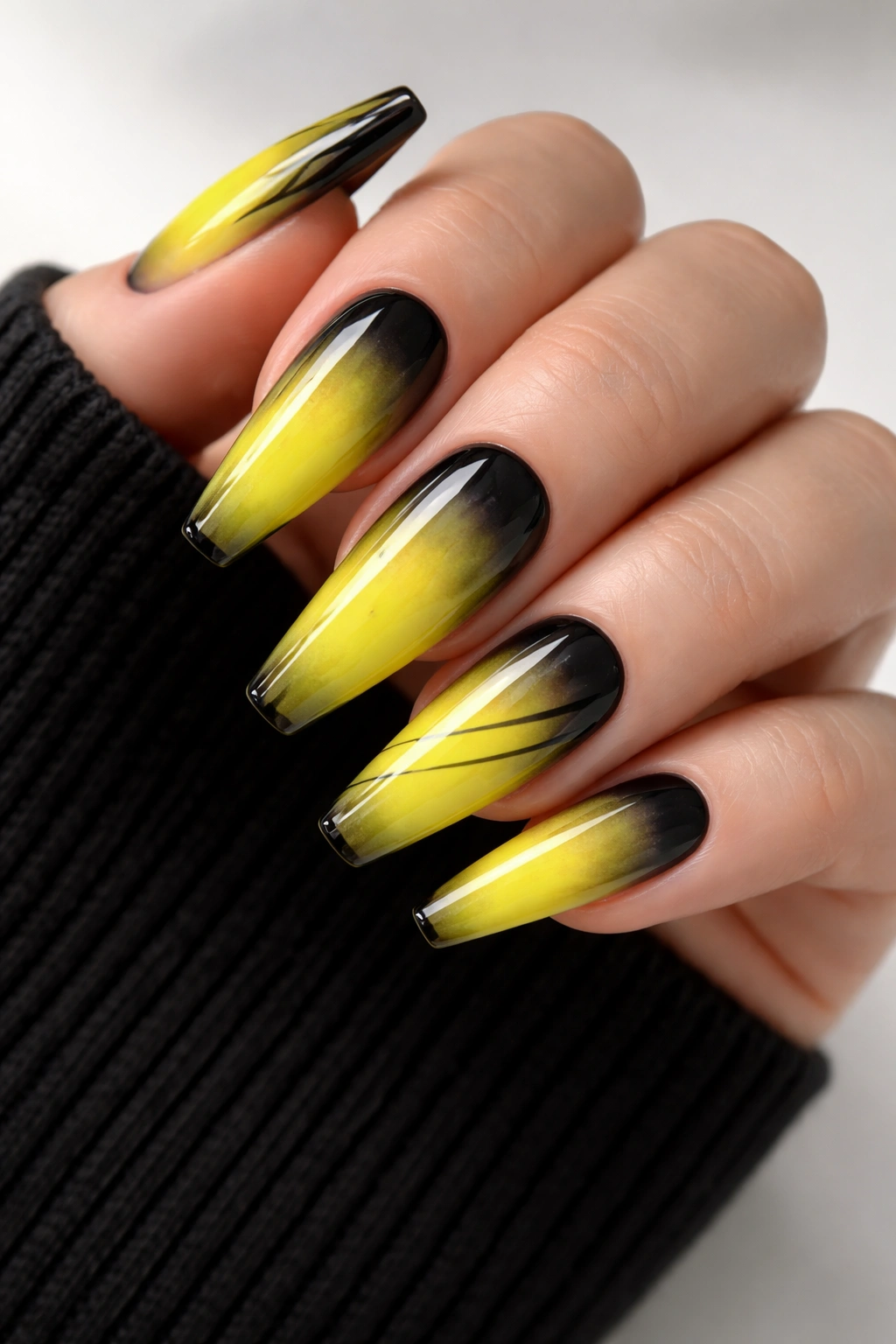 Close-up of yellow ombre coffin nails with black smoked edges and graphic lines on bare hand
