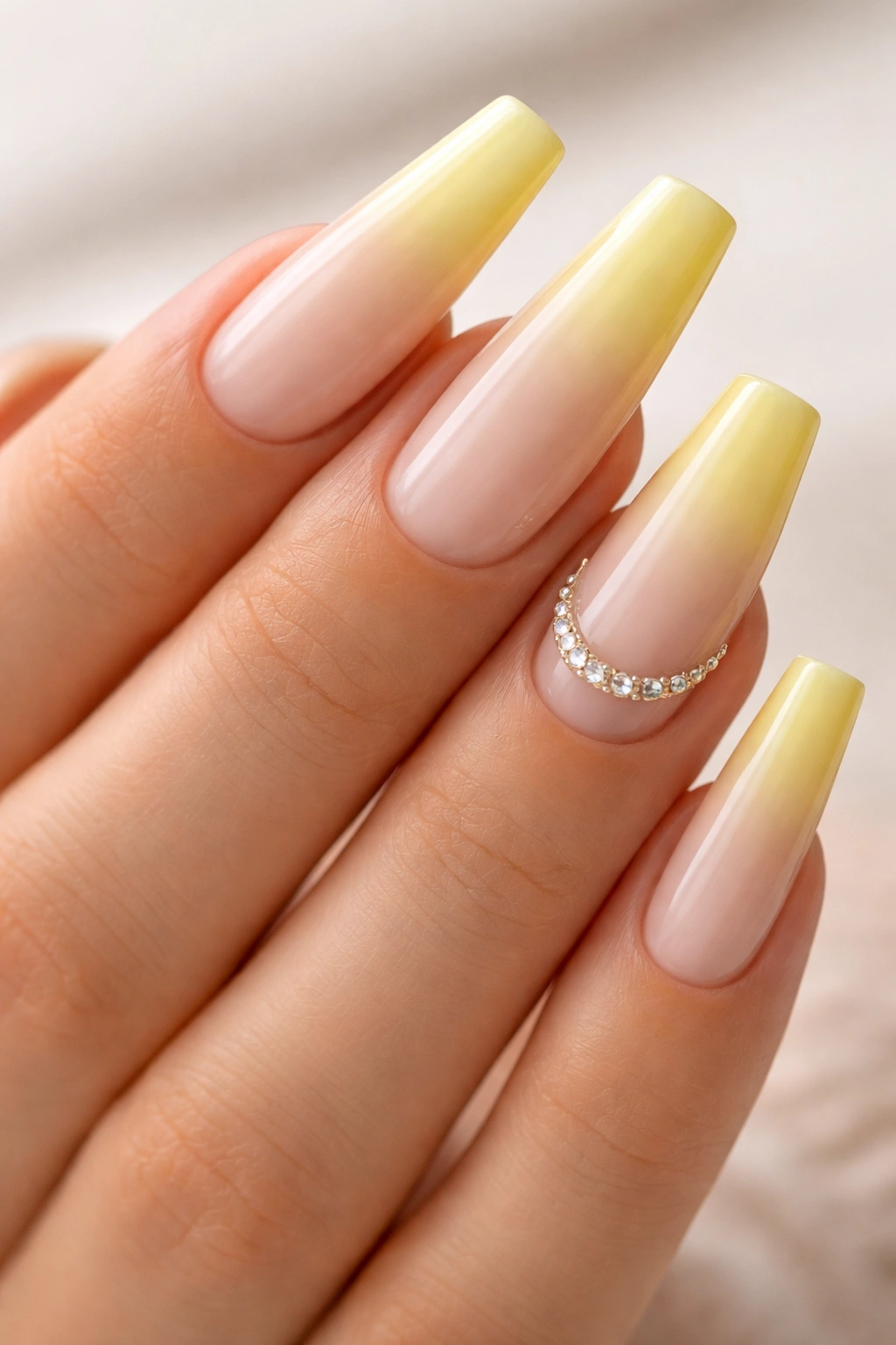 Close-up of yellow ombre coffin nails with rhinestone crescent near cuticle on accent nail